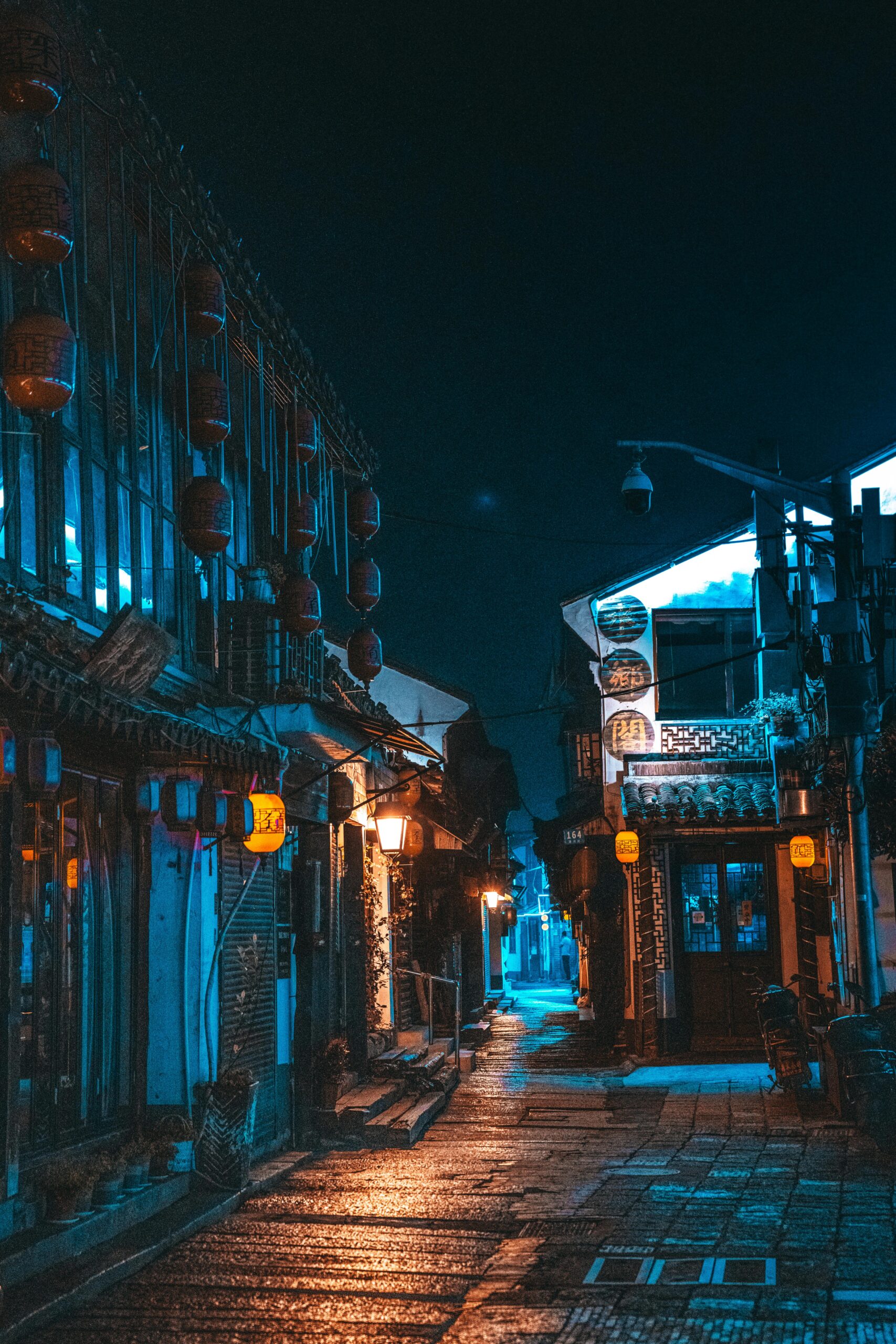 A quaint urban street at night, adorned with glowing traditional lanterns, creates a serene ambiance.