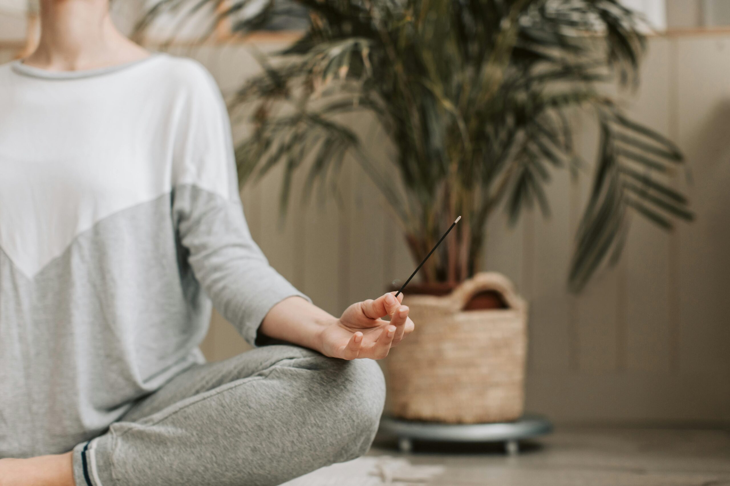 Woman meditating indoors holding incense, promoting relaxation and calm.